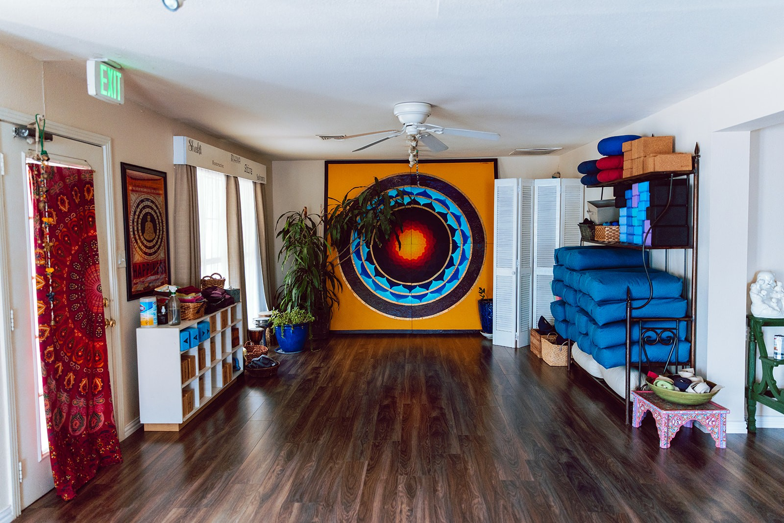 Wide view of the open practice room with the round mandala mural and stacked blue bolsters