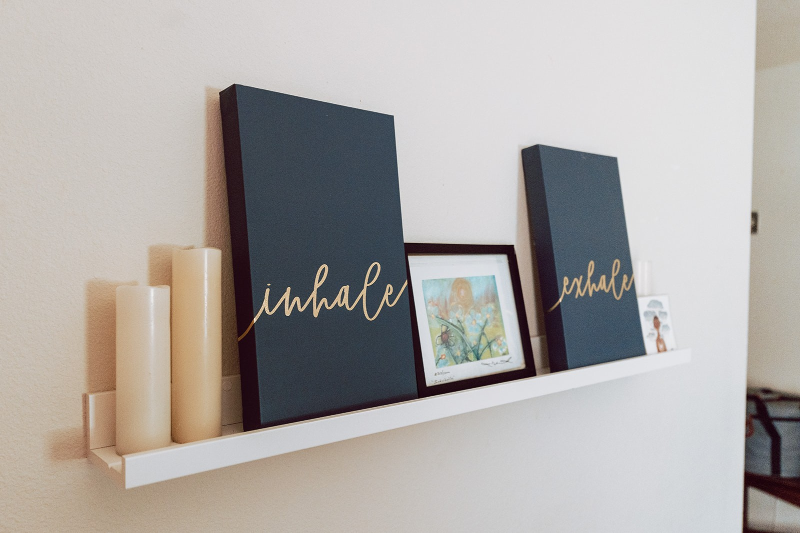 Shelf with candles and inhale and exhale canvases in gold lettering